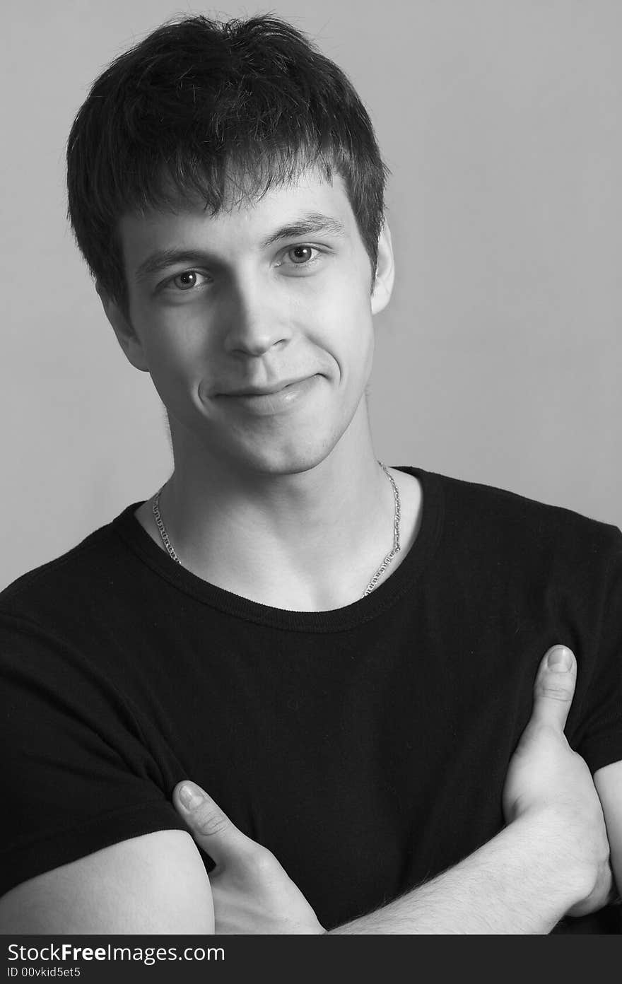 The young man in a black T-shirt friendly smiles. The young man in a black T-shirt friendly smiles