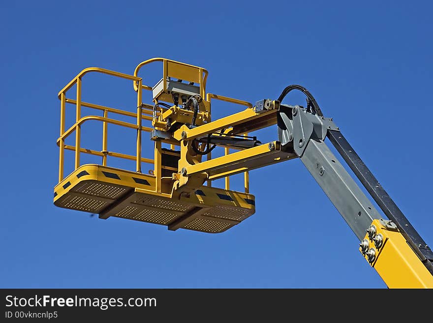 Yellow construction crane basket against blue sky.