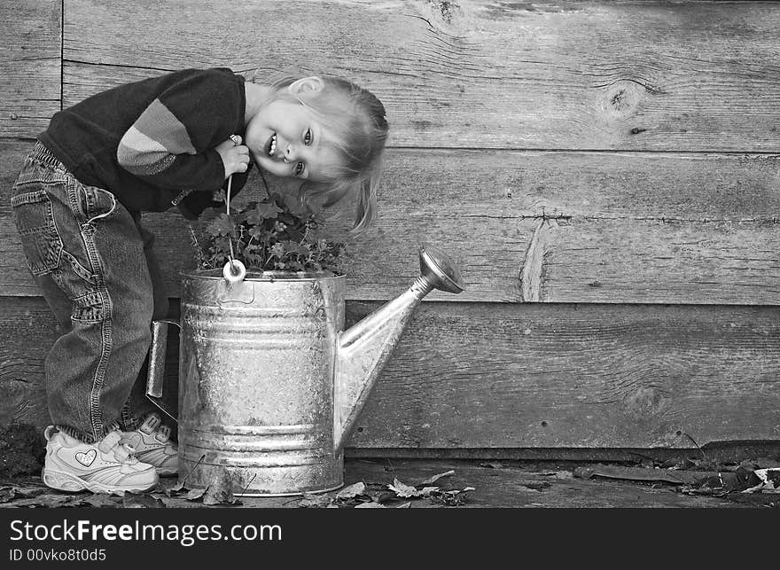 Little girl with watering can by an old barn. Little girl with watering can by an old barn.