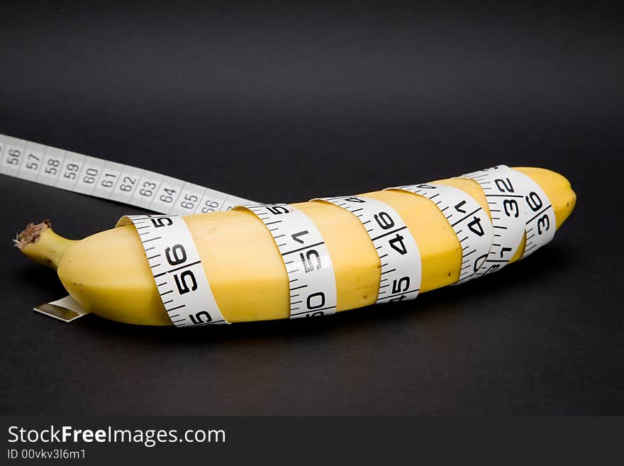 A banana with a tape measure wrapped around it in a spiral isolated on a black background. A banana with a tape measure wrapped around it in a spiral isolated on a black background.