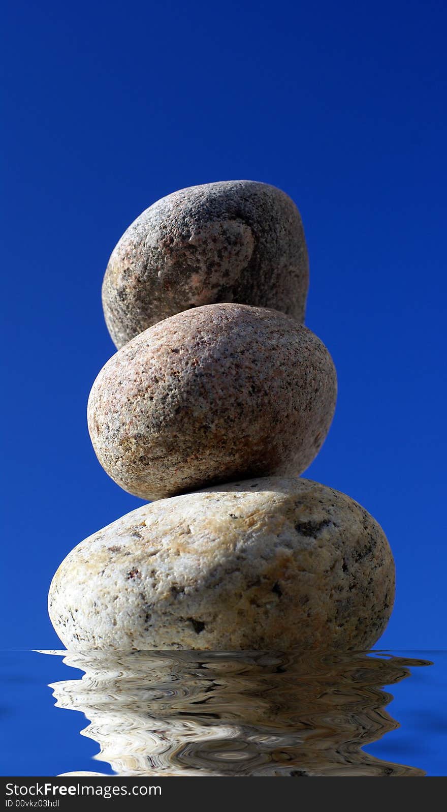 Stack of pebbles and reflection in water with blue sky background