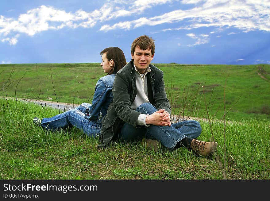 Guy and girl sits on a grass on a background of the sky