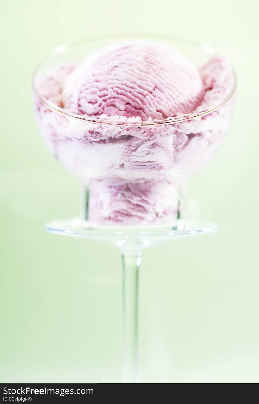 A scoop of raspberry ice cream in a glass cup on a pedestal. Green background. A scoop of raspberry ice cream in a glass cup on a pedestal. Green background