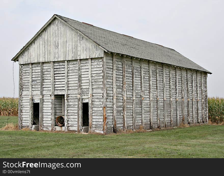 An old corn crib with a corn field behind it.