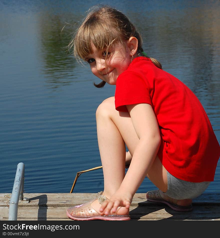 Smiling pretty little girl sitting on the river pier. Smiling pretty little girl sitting on the river pier