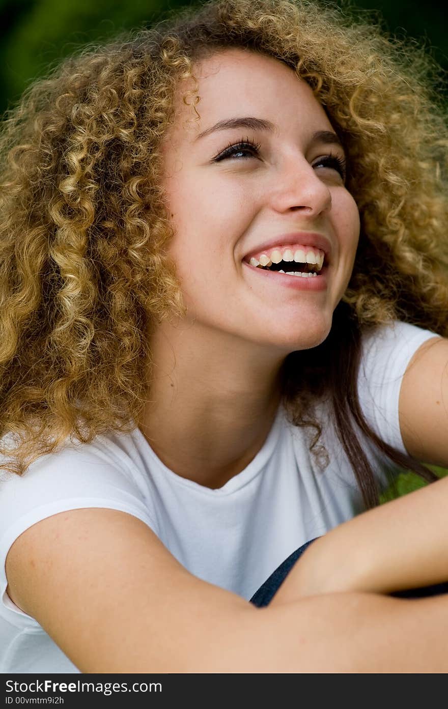 A young attractive woman sitting outside in the park laughing. A young attractive woman sitting outside in the park laughing