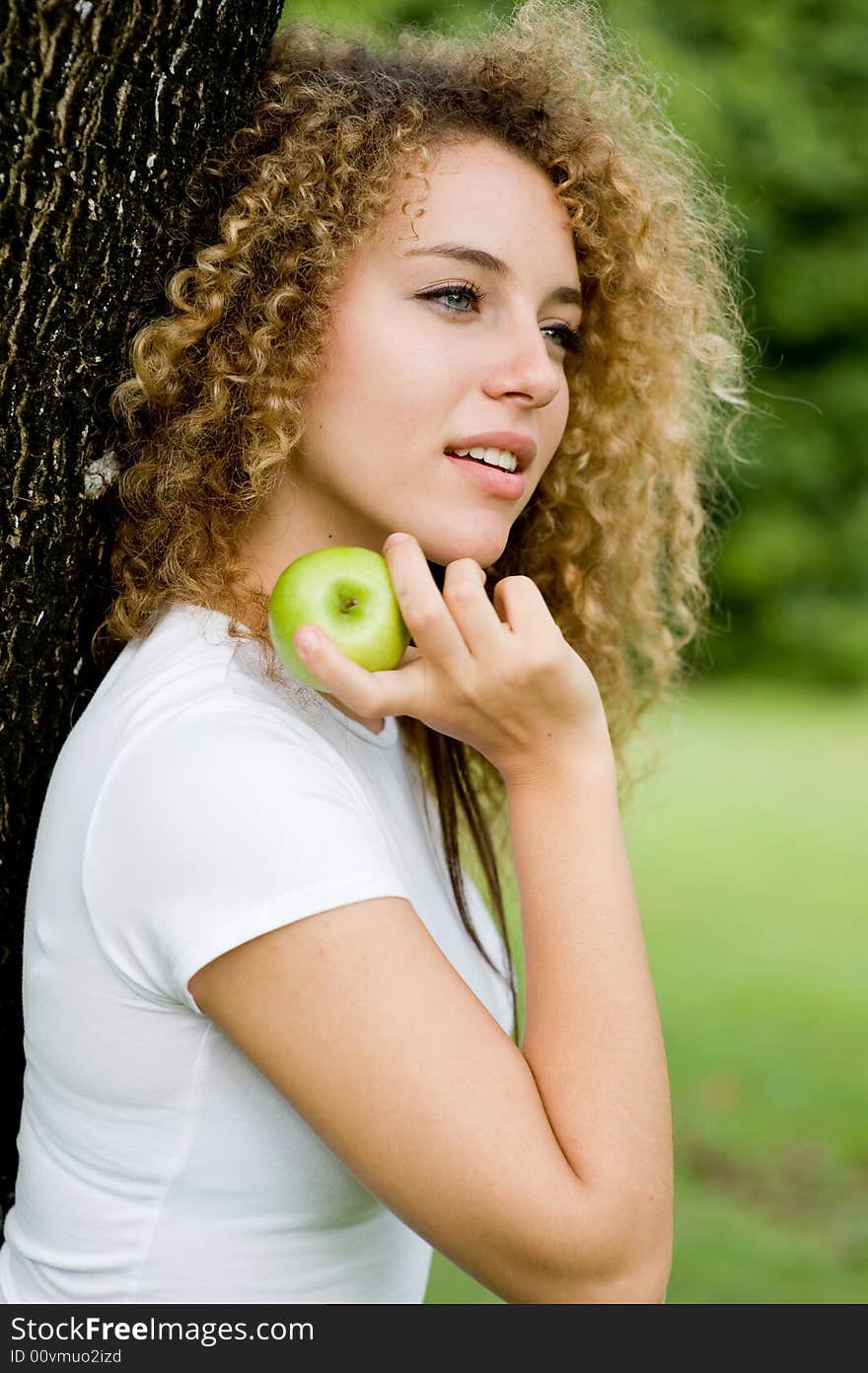 A pretty young woman outside in a park holding a green apple. A pretty young woman outside in a park holding a green apple