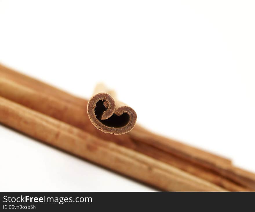 Horizontal image of piled cinnamon sticks flowing from one side of the frame to the other, with a single stick placed on top.  Curves of the single stick resemble a heart.