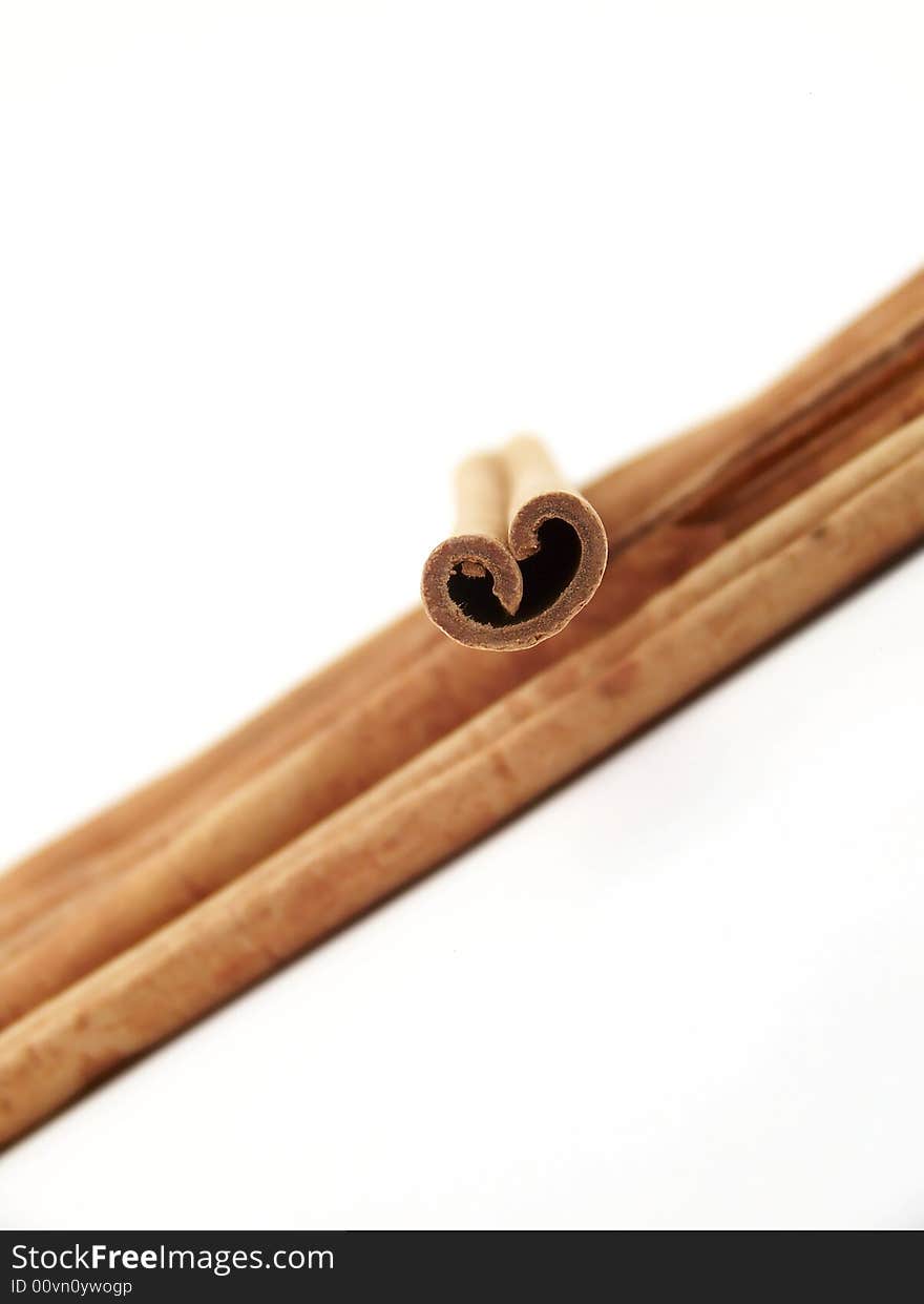 Vertical image of a pile of cinnamon sticks flowing from one side of the frame to the other, with a single stick placed on top.  Curves of the single stick resemble a heart.