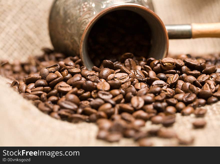 Cezve with freshly roasted coffee beans on sackcloth. Shallow depth of field. Focus on center of image