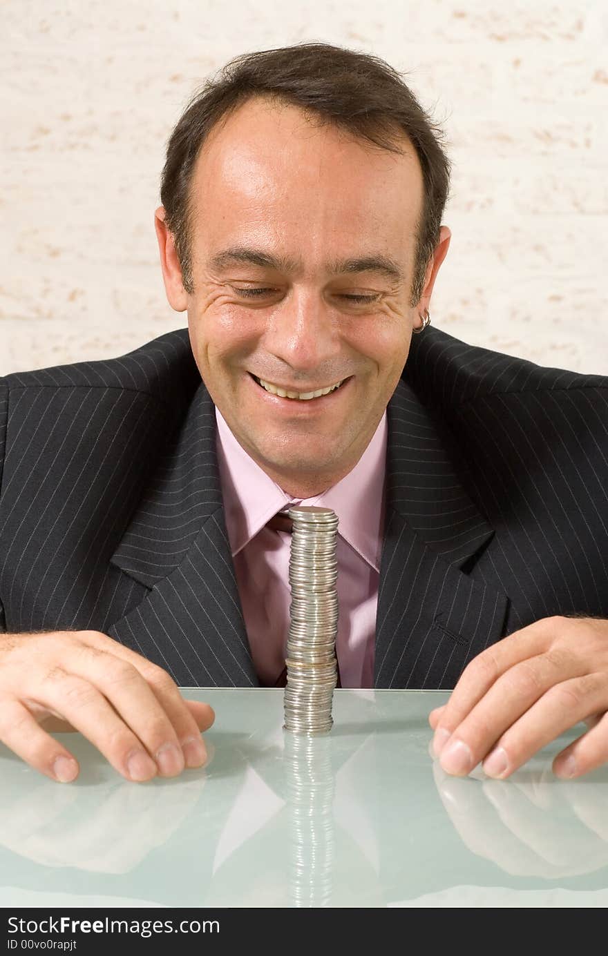 A shot of a smiling businessman looking at a stack of quarters on class desk. A shot of a smiling businessman looking at a stack of quarters on class desk.