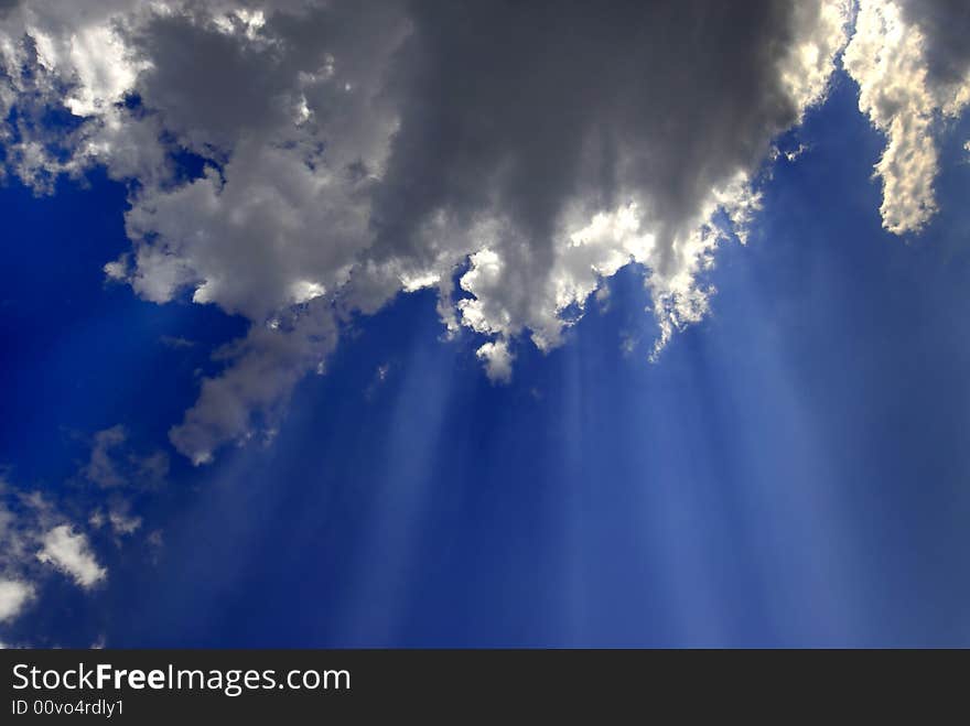 View of white and gray storm clouds in blue sky with rays of light. View of white and gray storm clouds in blue sky with rays of light