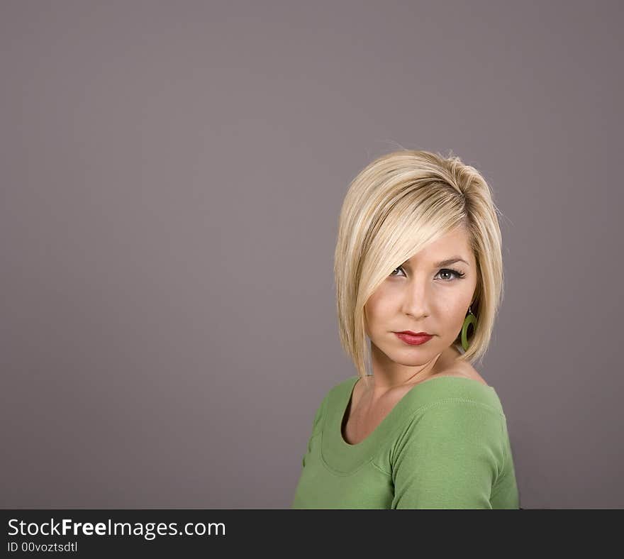 A blonde in a green blouse turned to side with hair over one eye. A blonde in a green blouse turned to side with hair over one eye