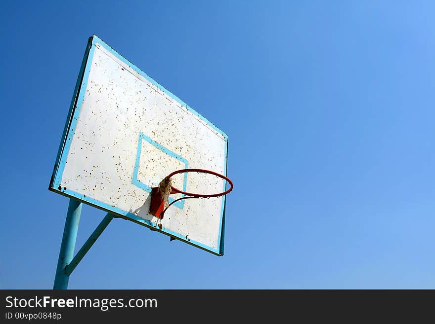 Old basketball hoop on clear blue sky.