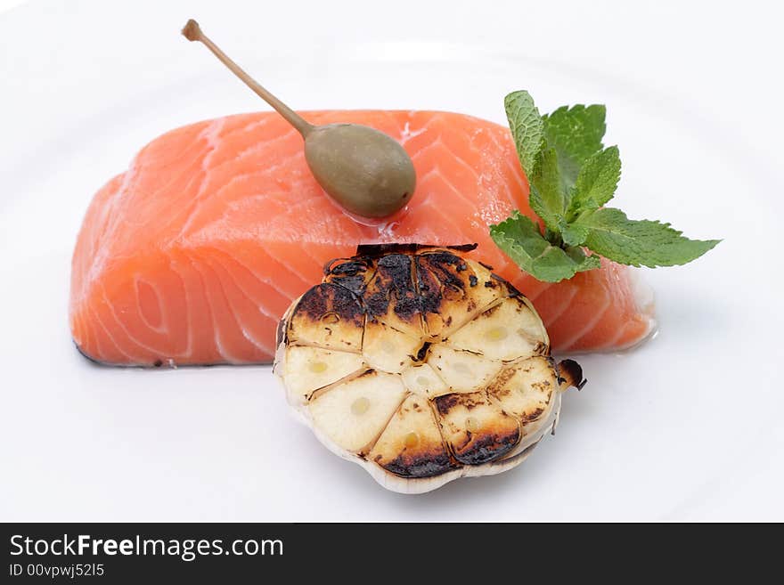 Fresh salmon, garlic and green on a plate. Isolated on a white background. Fresh salmon, garlic and green on a plate. Isolated on a white background