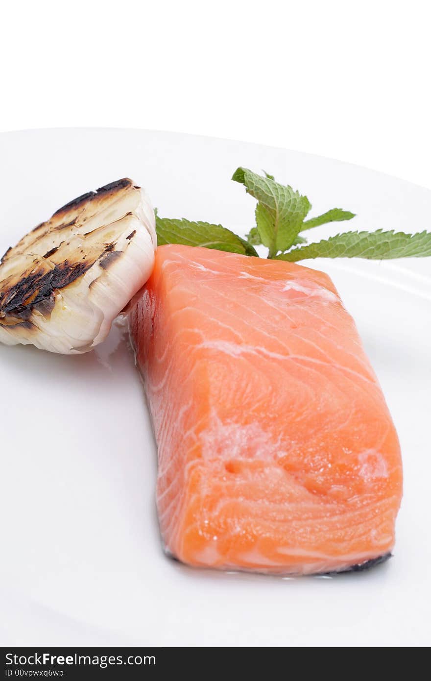 Fresh salmon, garlic and green on a plate. Isolated on a white background. Fresh salmon, garlic and green on a plate. Isolated on a white background