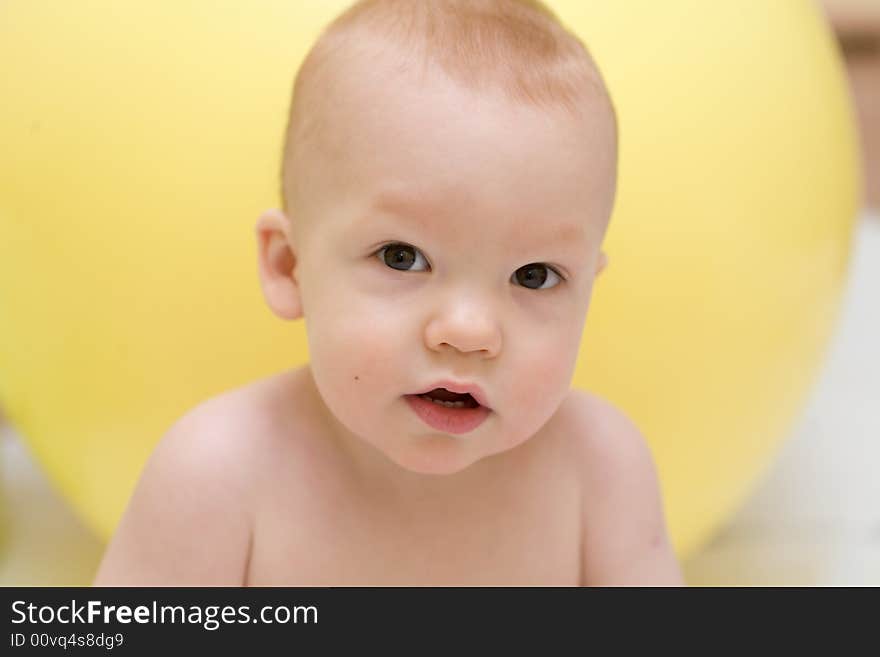 Baby with interest looking at camera against the yellow gymnastic ball