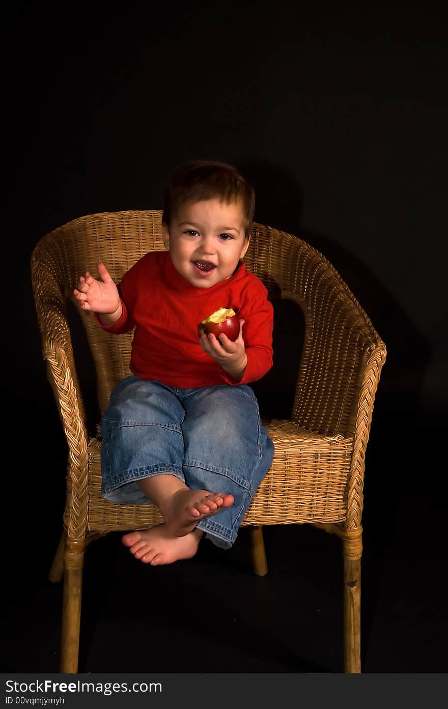 Boy sitiing in armchair, eating apple and shouting (isolated on black)