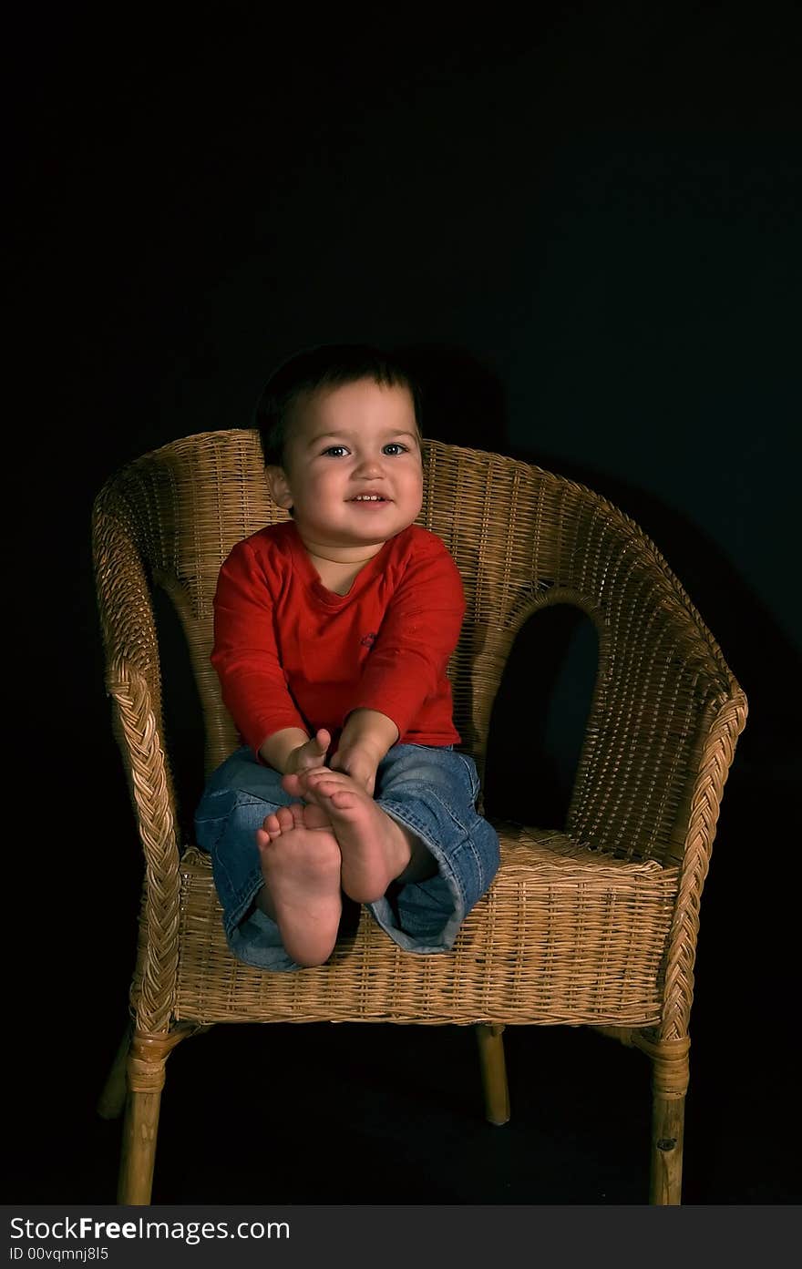 Happy boy siiting on cane-chair isolated on black