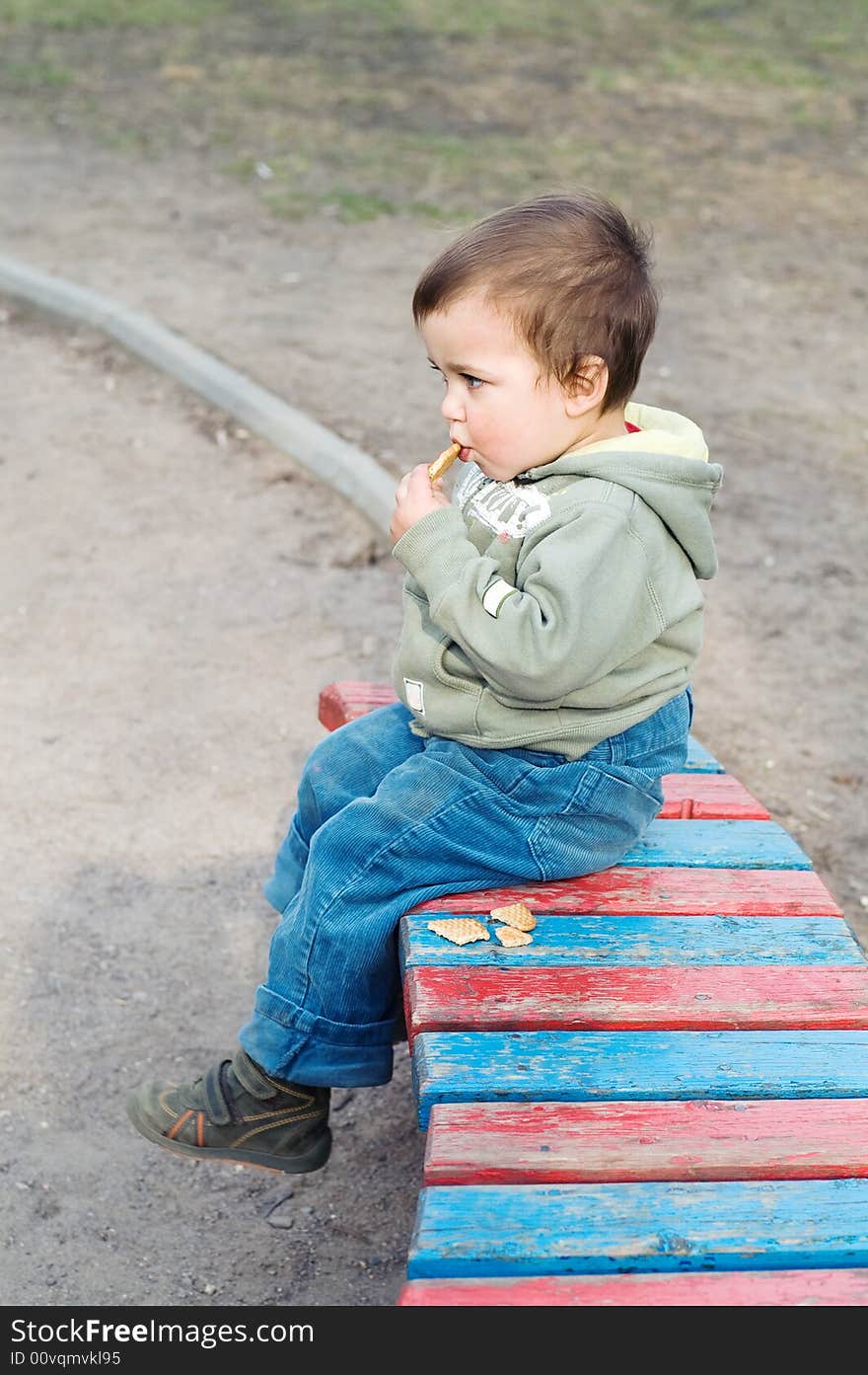 Boy eating cookie and relaxing (sitting on bench in park)