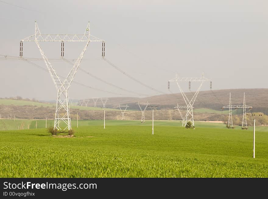 Many electricity pylons with wire in the green fields. Many electricity pylons with wire in the green fields