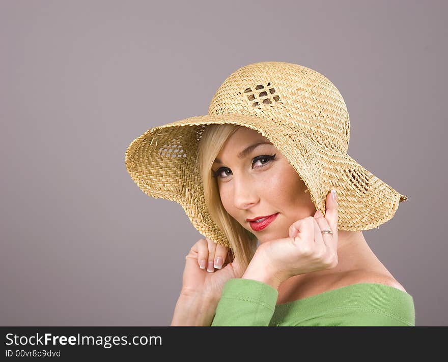 A blonde in a green blouse and a straw hat pulling the brim over her ears. A blonde in a green blouse and a straw hat pulling the brim over her ears