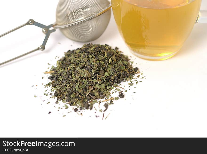 Green tea with strainer and leaves on a white surface. Green tea with strainer and leaves on a white surface