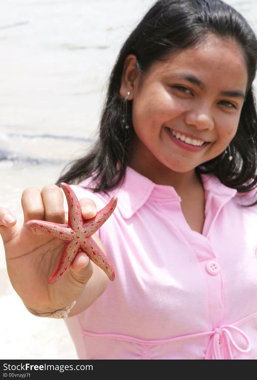 Asian girl at the beach holding up a red starfish.