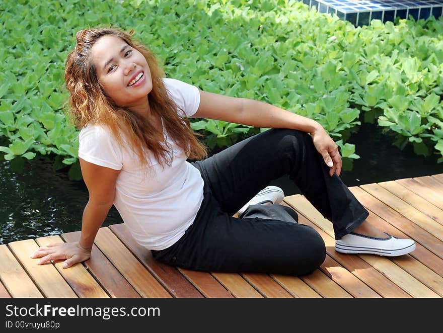 Attractive young Thai girl sitting on a wooden deck.