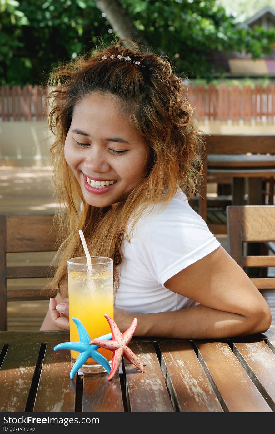 Pretty Thai woman enjoying a glass of orange juice at a cafe.