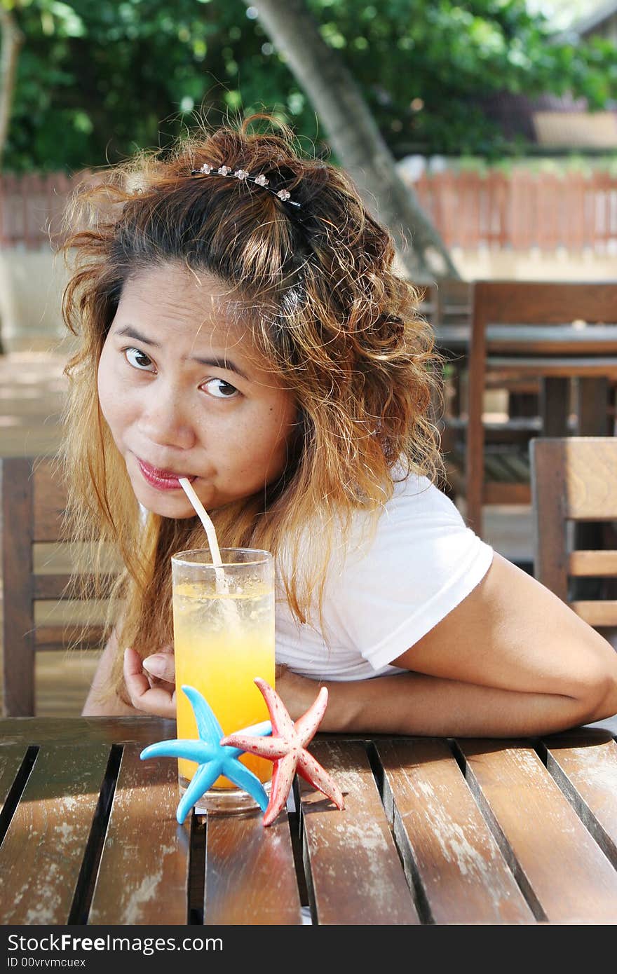 Pretty Thai woman enjoying a glass of orange juice at a cafe.