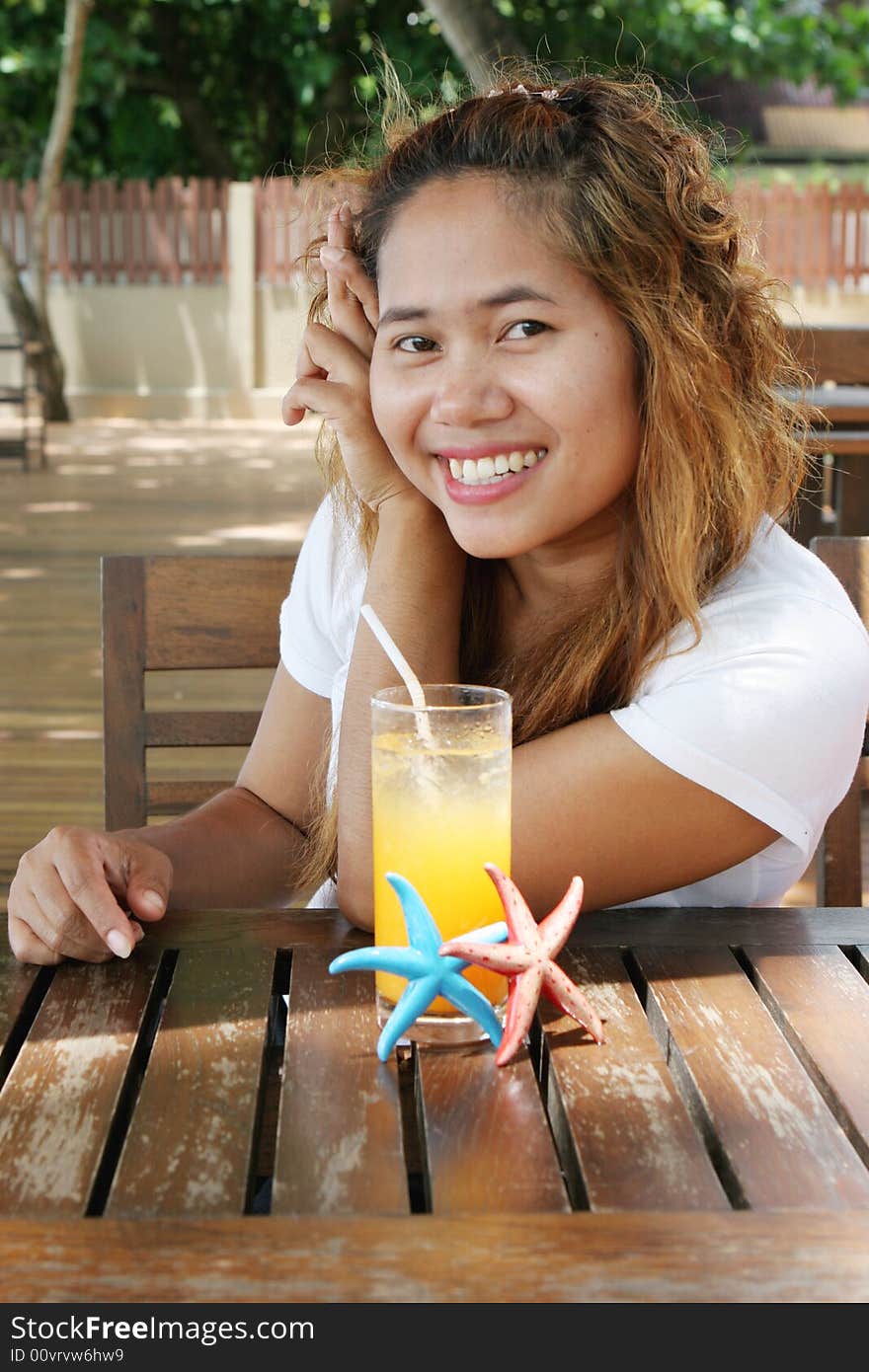 Pretty Thai woman enjoying a glass of orange juice at a cafe.