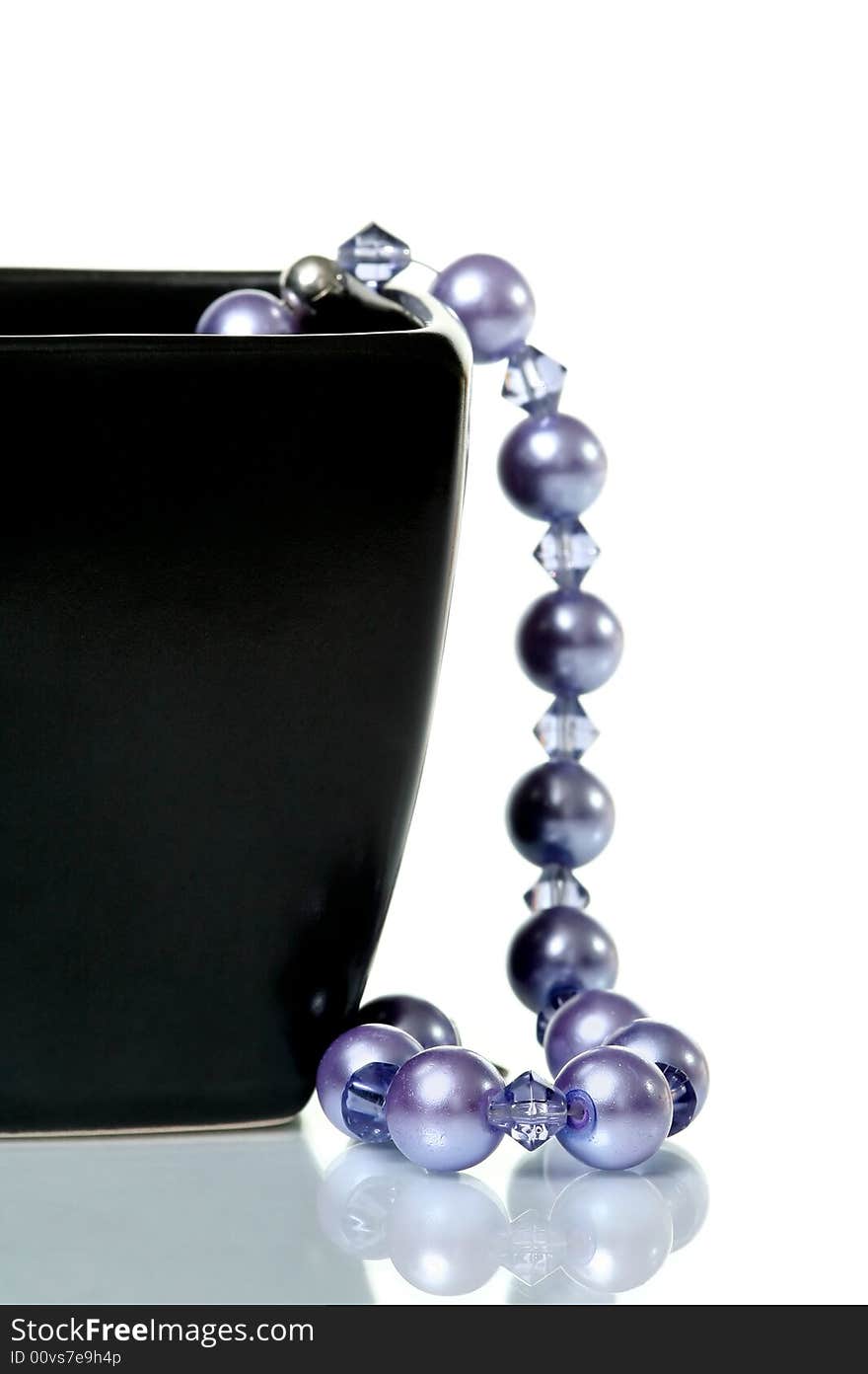 Purple necklace hanging from black glass bowl on white background. Purple necklace hanging from black glass bowl on white background