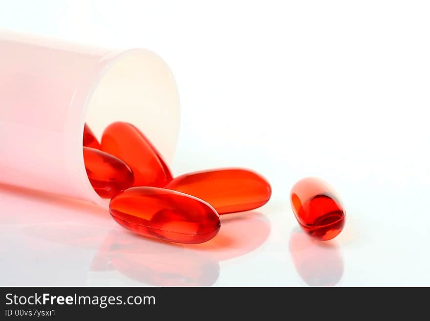 Translucent orange capsules with pill bottle on white background