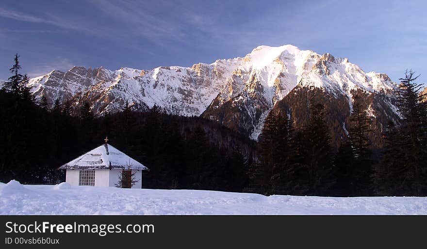 A winter landscape with a mountain peak and a small house