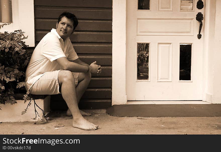 Black and white of a man sitting next to a doorway with tropical island type architecture. Black and white of a man sitting next to a doorway with tropical island type architecture