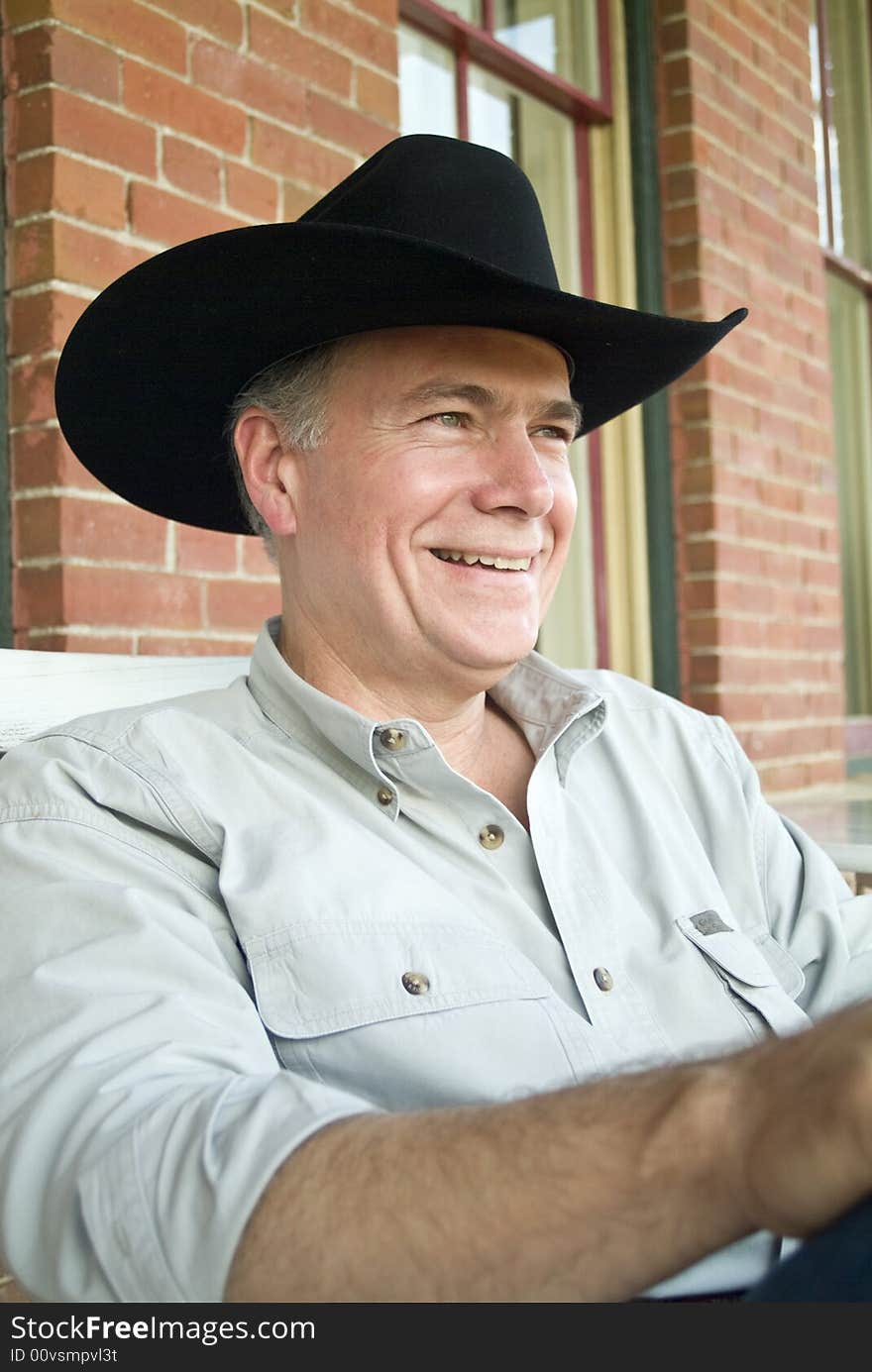 A man sitting on a porch wearing a cowboy hat with a big happy smile on his face. A man sitting on a porch wearing a cowboy hat with a big happy smile on his face.