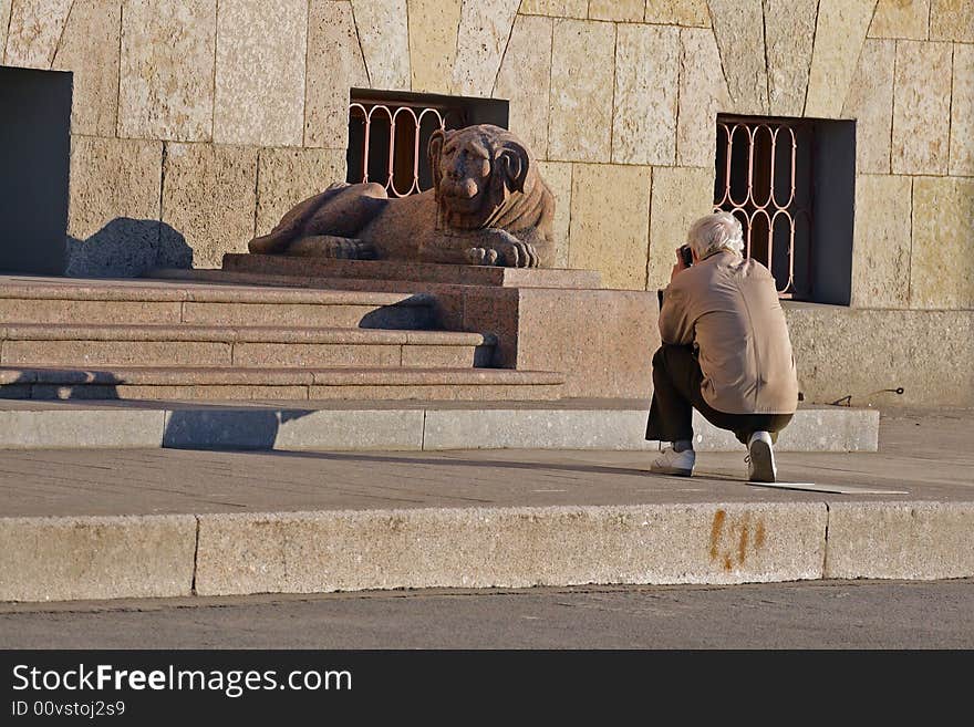 Hiker take a photograph granite sculpture lion on river's Neva embankment in Saint-Petersburg, Russia.