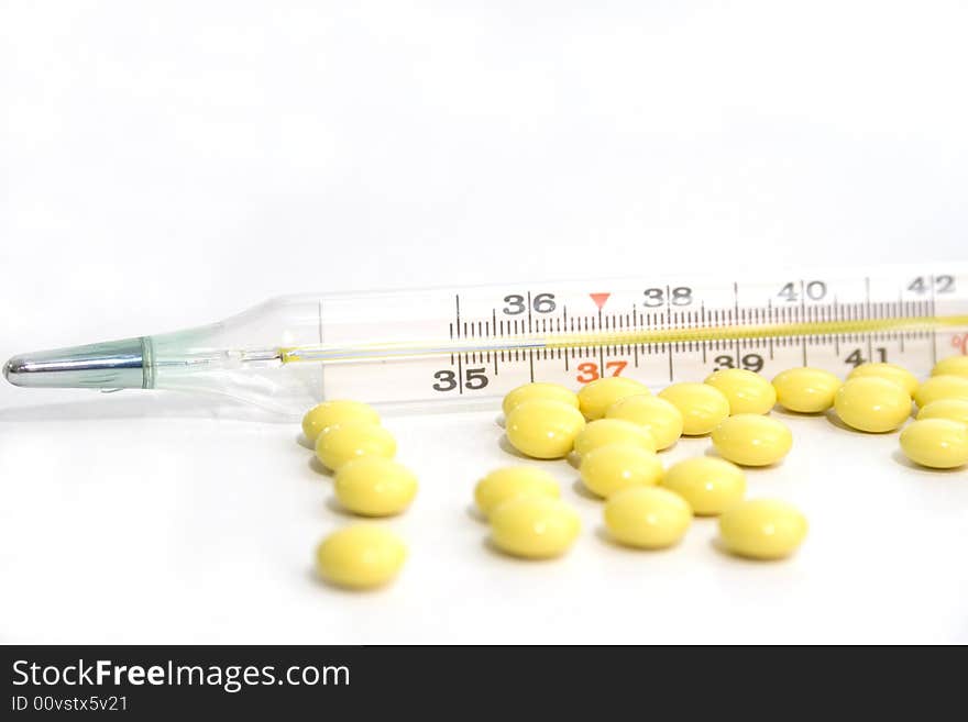 Thermometer and yellow tablets on the white background. Thermometer and yellow tablets on the white background