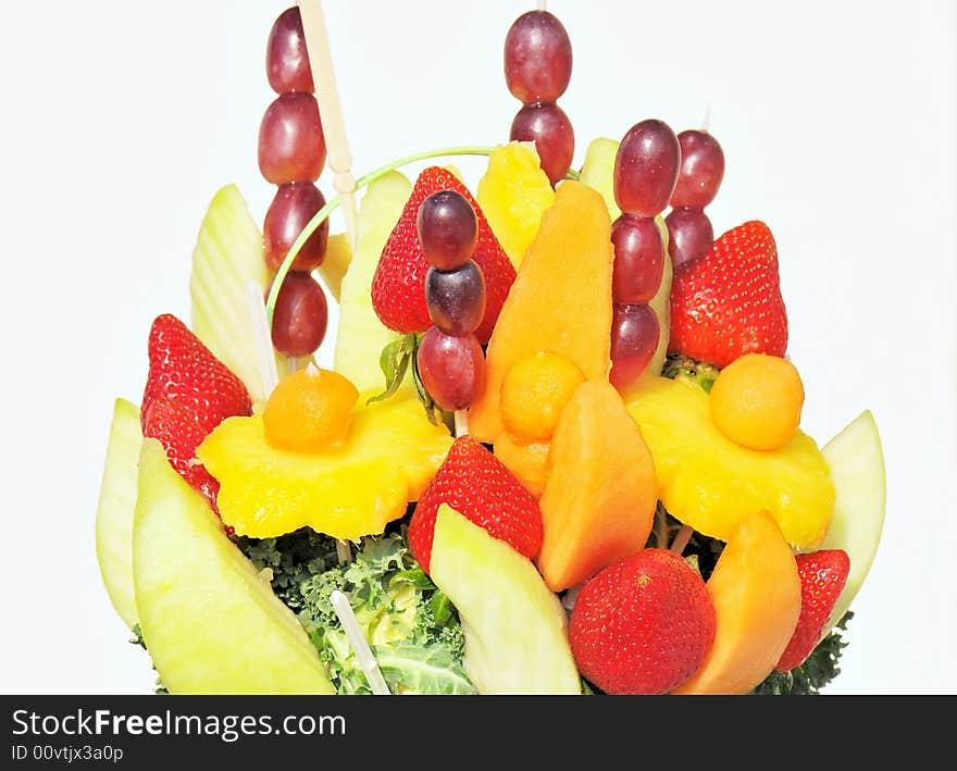 A closeup view of a colorful display and arrangement of fruit including strawberries, pineapple, melons, and grapes on sticks and embedded in lettuce. A closeup view of a colorful display and arrangement of fruit including strawberries, pineapple, melons, and grapes on sticks and embedded in lettuce.