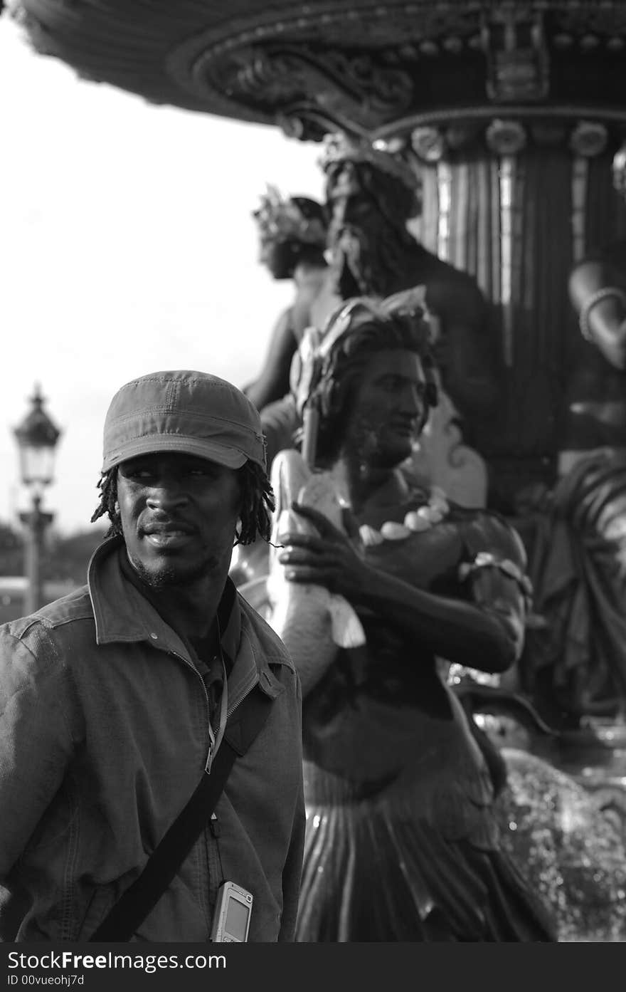 Black and white picture of a young african man near of a fountain located in Paris. Black and white picture of a young african man near of a fountain located in Paris.