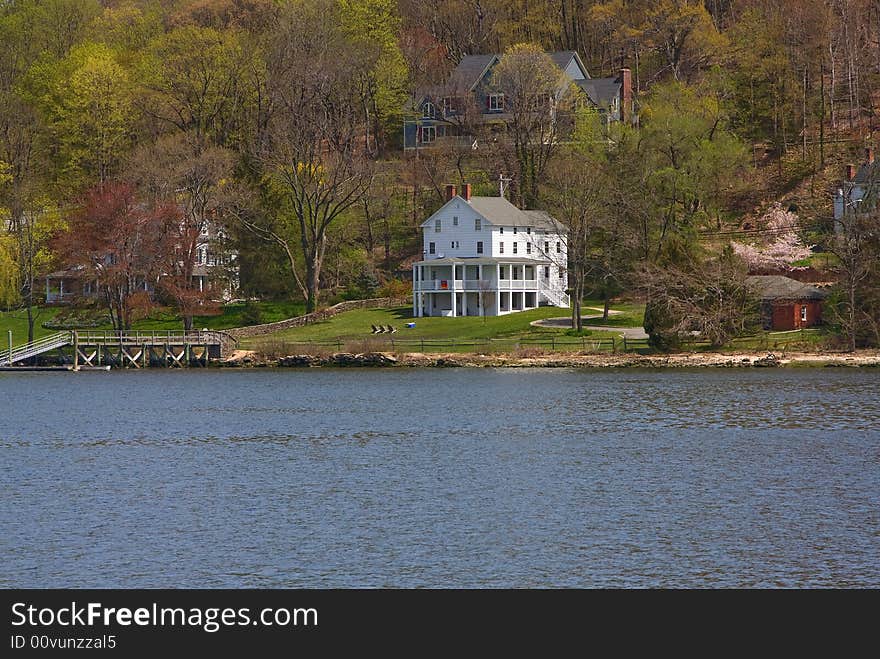 A remotely located white Victorian/Colonial mansion on the water and in the woods on a spring day. A remotely located white Victorian/Colonial mansion on the water and in the woods on a spring day.