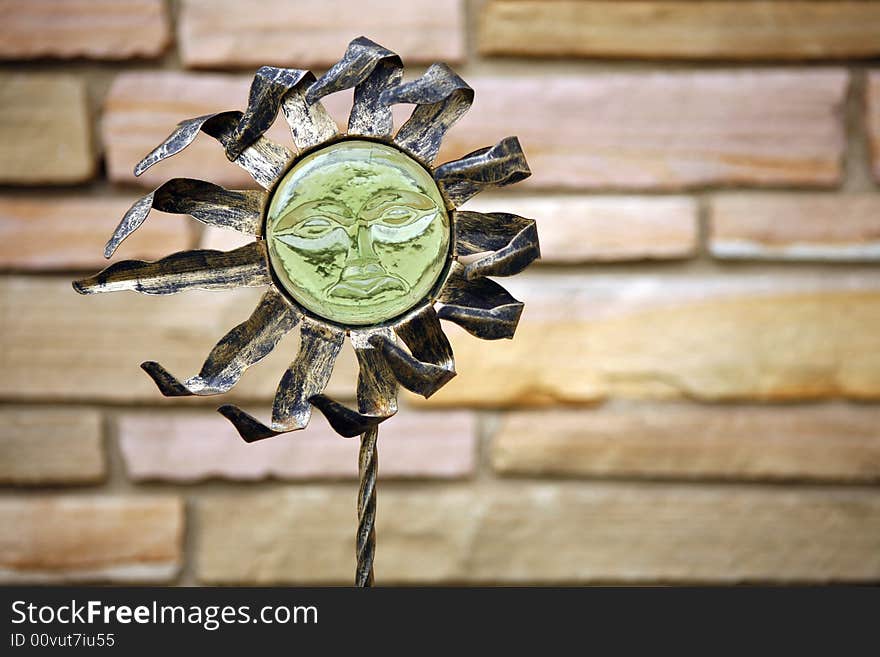 Decorative sun sits outside in front of stone wall.