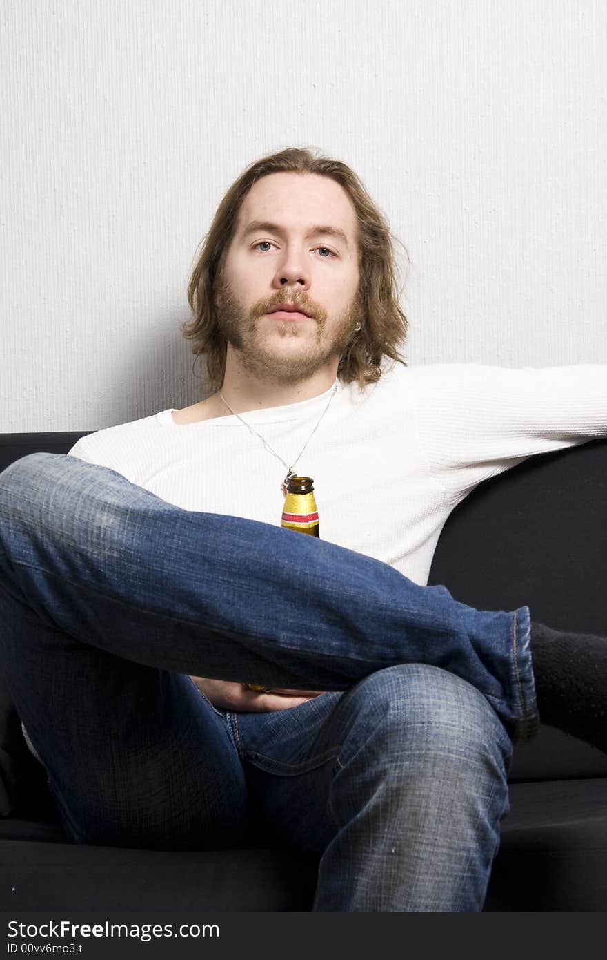 Young man with bottle of beer sitting on the sofa