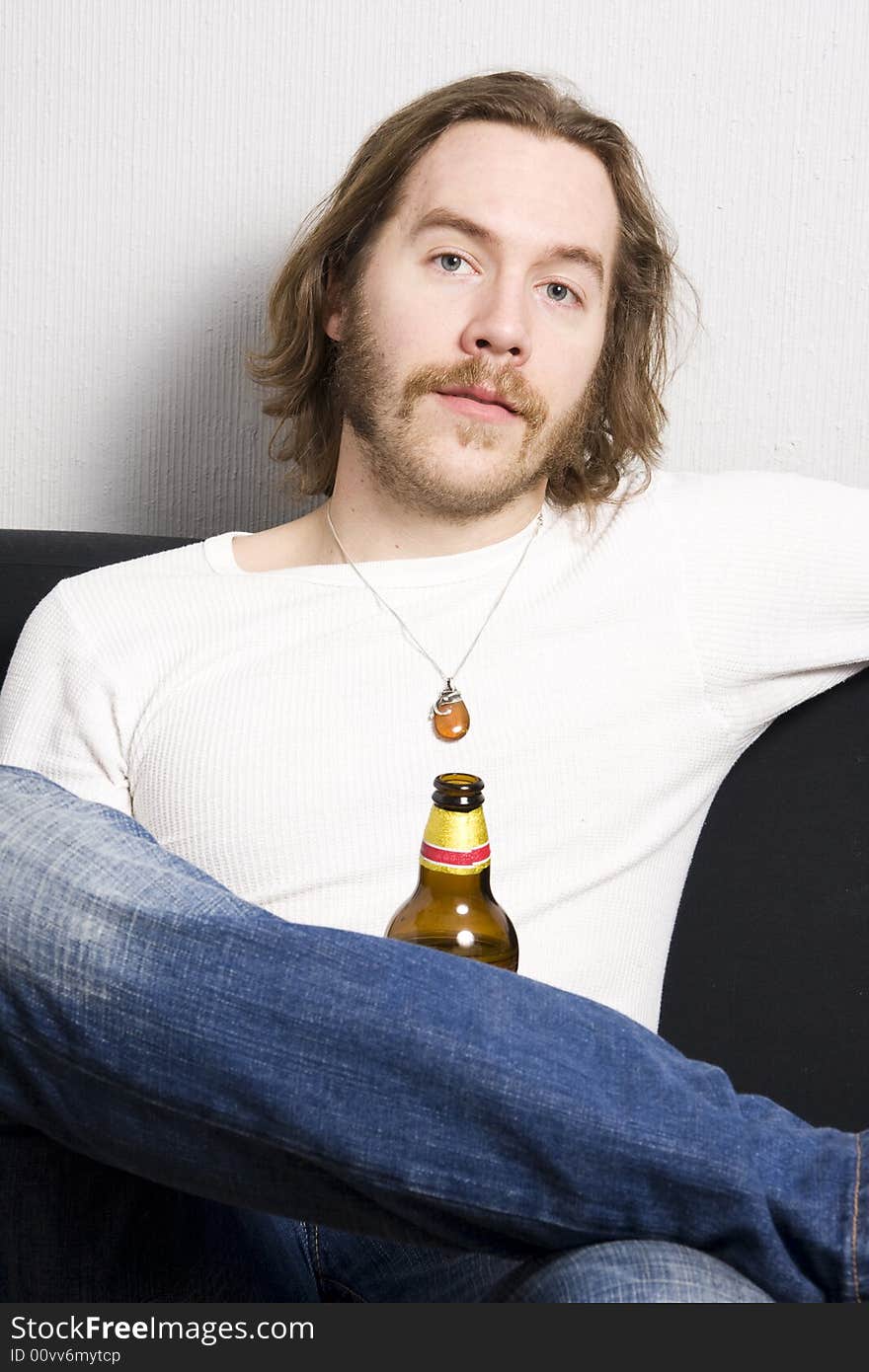 Young man with bottle of beer sitting on the sofa