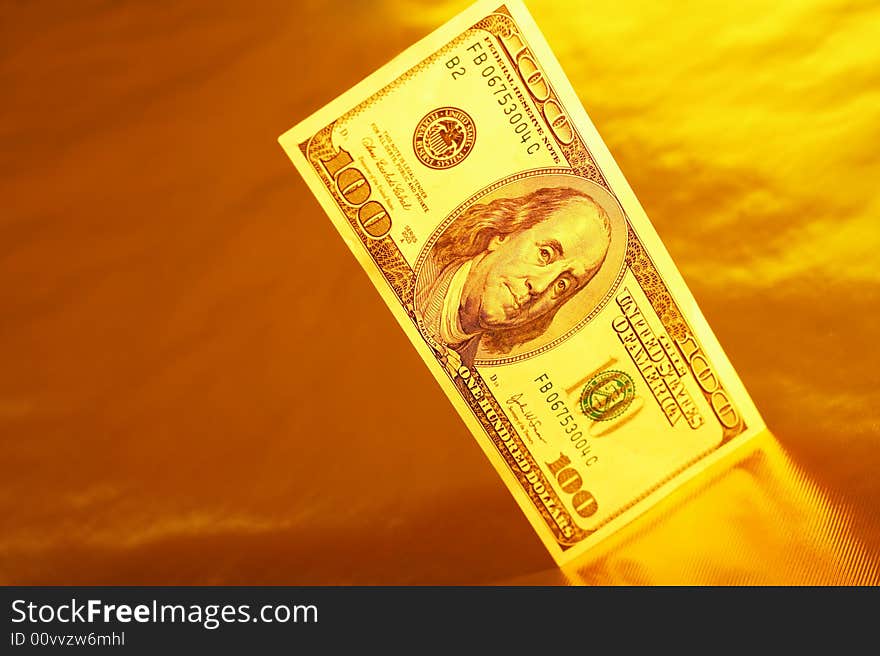 Hundred dollar denomination stands on a reflecting surface of a gold background. Hundred dollar denomination stands on a reflecting surface of a gold background