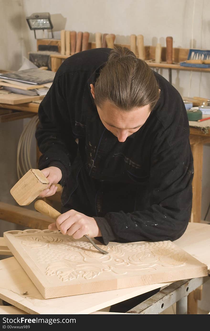 Carpenter cutting in his workshop with chisel and wooden hammer