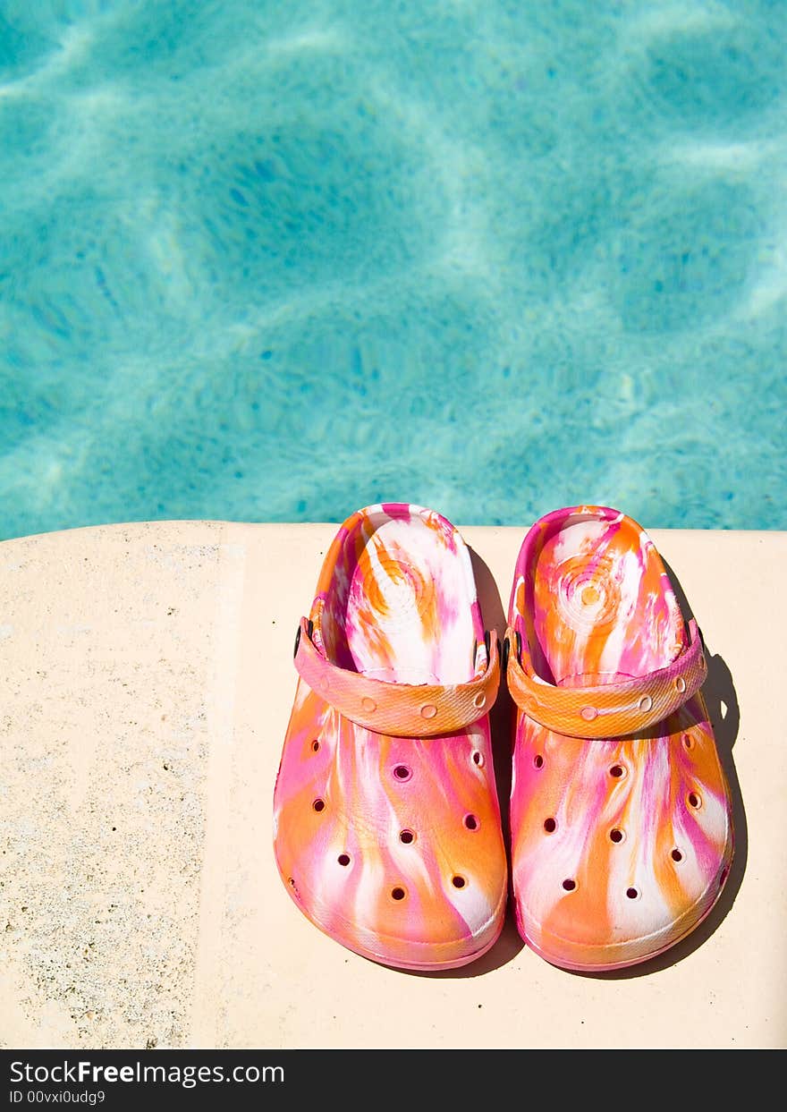 Brightly colored sandals by the side of swimming pool.