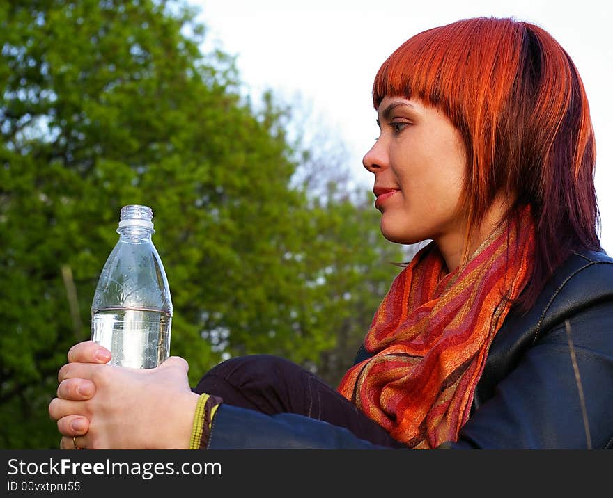 The beautiful young girl drinks water on a background of the sky