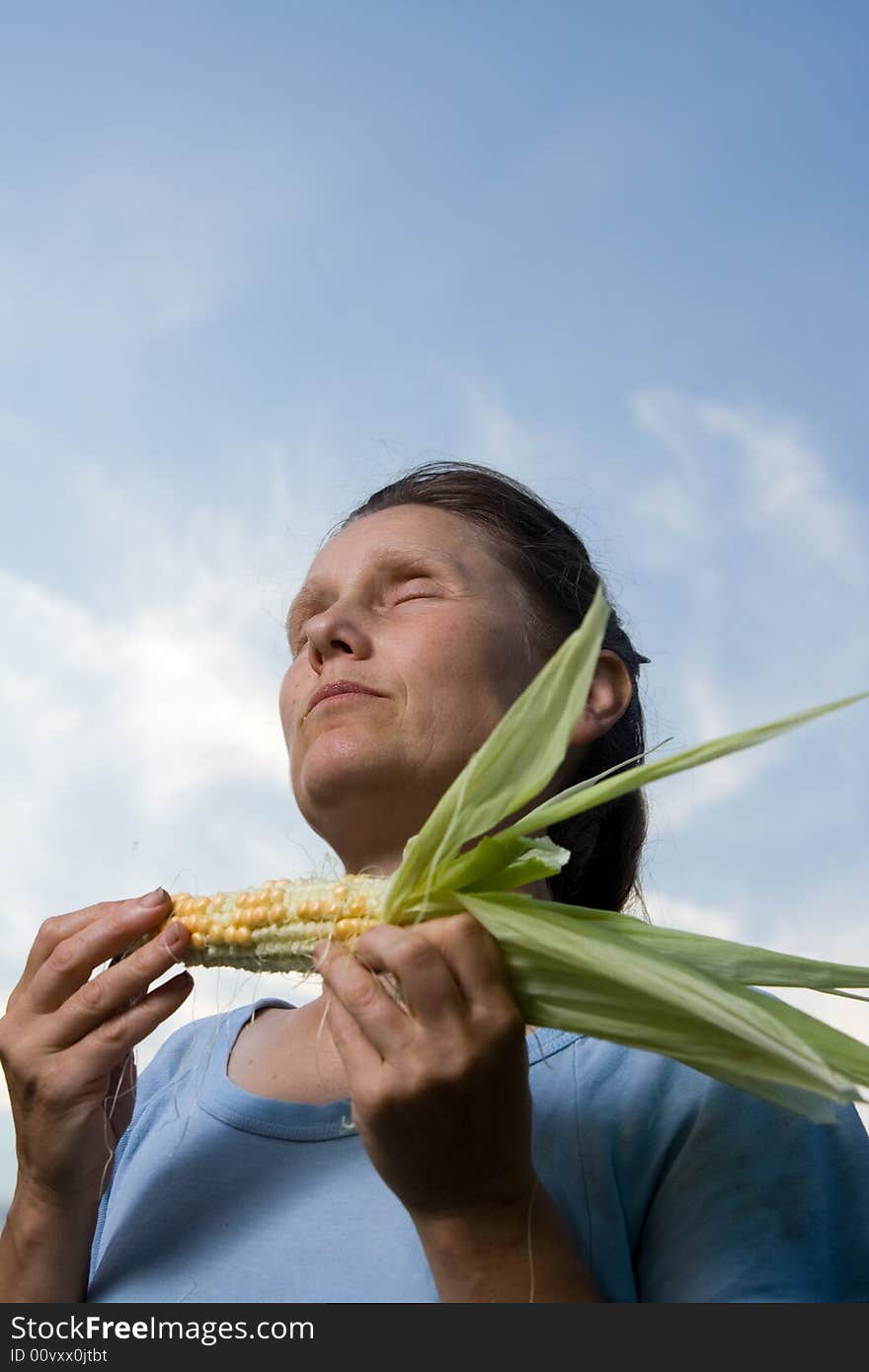 Middle adult woman with corncob in hands tasting it and enjoying.